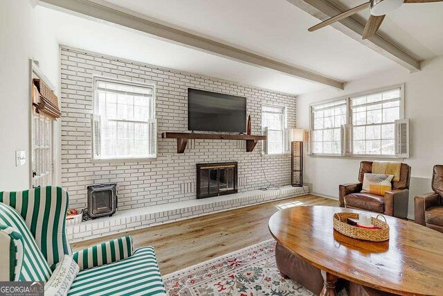 living room with beam ceiling, a fireplace, brick wall, and wood finished floors