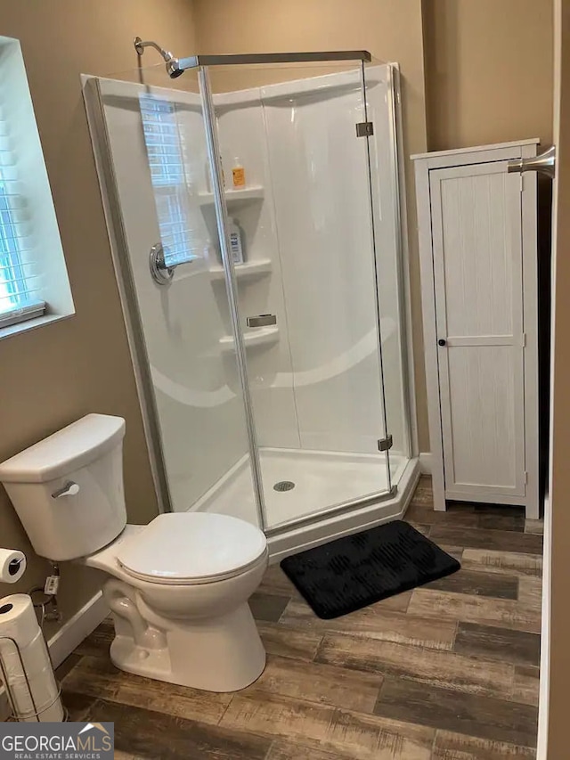 bathroom featuring toilet, wood finished floors, and a stall shower