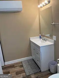 half bath featuring baseboards, toilet, an AC wall unit, wood finished floors, and vanity