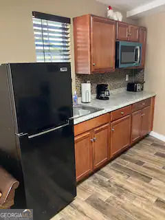 kitchen featuring light wood finished floors, freestanding refrigerator, a sink, light countertops, and backsplash