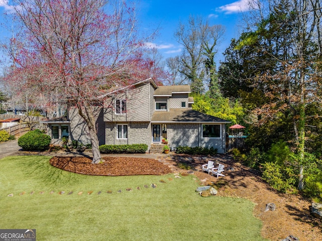 view of front of house with fence, roof with shingles, a front lawn, and stone siding