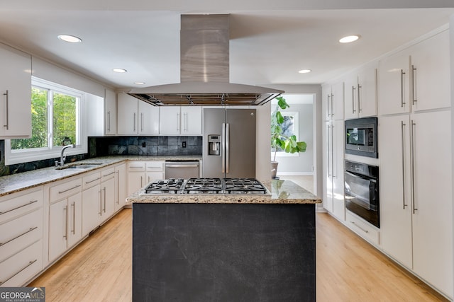 kitchen with a sink, backsplash, stainless steel appliances, light wood-style floors, and island range hood