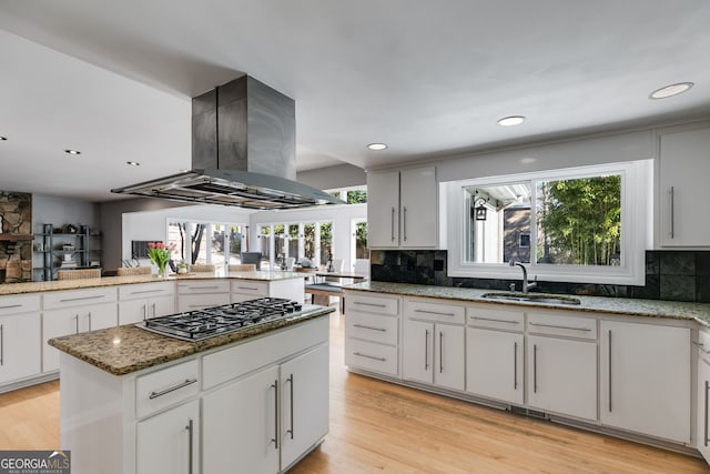 kitchen featuring stainless steel gas stovetop, a sink, island exhaust hood, and tasteful backsplash