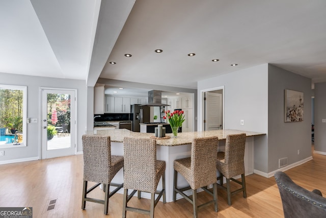 kitchen with a kitchen bar, a peninsula, refrigerator with ice dispenser, and island exhaust hood