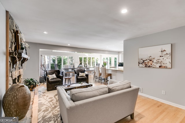 living room featuring a stone fireplace, recessed lighting, baseboards, and light wood finished floors