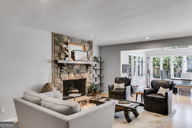 living area with a stone fireplace, light wood-style flooring, recessed lighting, and baseboards