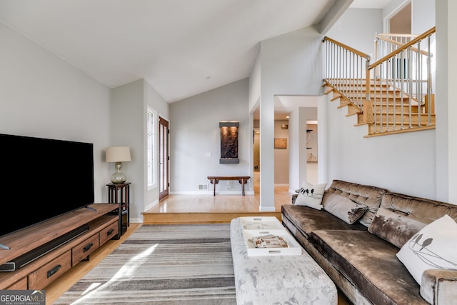 living room featuring high vaulted ceiling, baseboards, wood finished floors, visible vents, and stairway