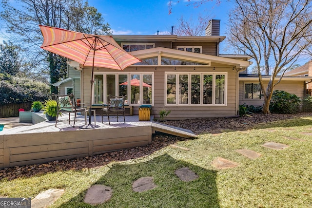 back of property with a lawn, a wooden deck, a chimney, and fence