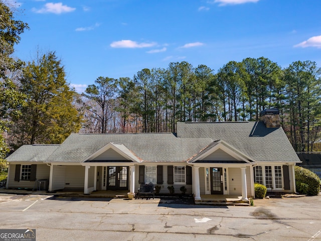 view of front of house featuring a porch, french doors, a chimney, and roof with shingles