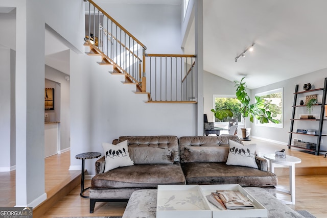 living area featuring high vaulted ceiling, track lighting, wood finished floors, stairway, and baseboards