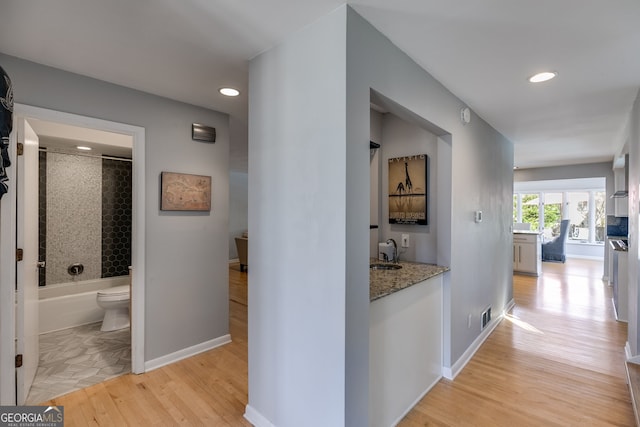 hallway with light wood-type flooring, visible vents, a sink, recessed lighting, and baseboards