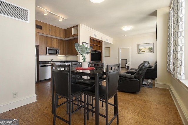 dining area with dark wood-type flooring, crown molding, and visible vents