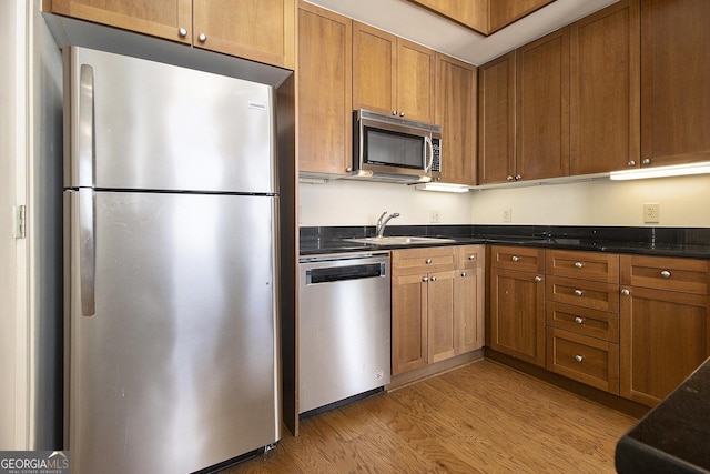 kitchen with a sink, dark stone counters, light wood-style floors, appliances with stainless steel finishes, and brown cabinetry