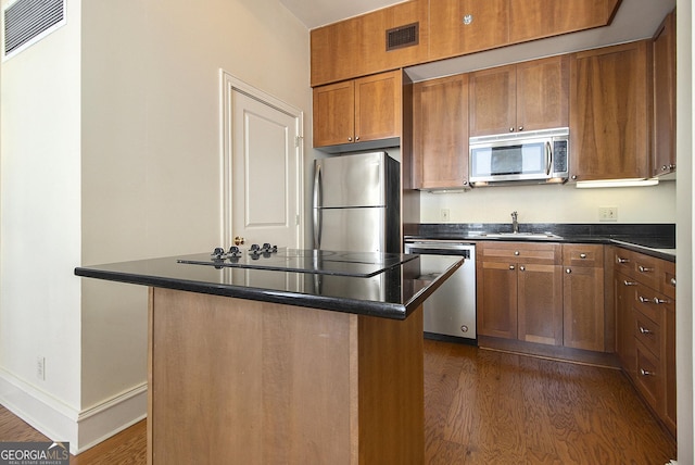 kitchen with visible vents, a sink, stainless steel appliances, dark wood-type flooring, and dark countertops