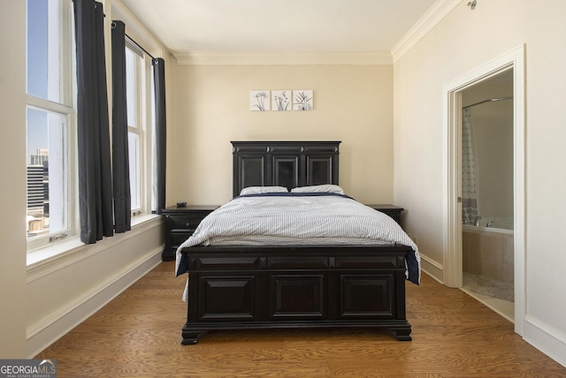 bedroom with wood finished floors, baseboards, ensuite bathroom, and ornamental molding