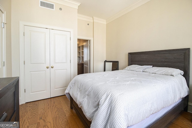 bedroom featuring a closet, visible vents, ornamental molding, and wood finished floors