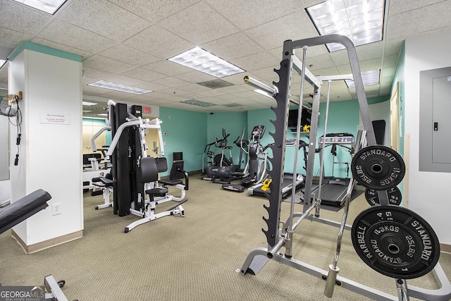 workout area featuring electric panel, a drop ceiling, and baseboards