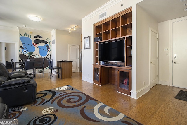 unfurnished living room featuring baseboards, wood finished floors, visible vents, and ornamental molding