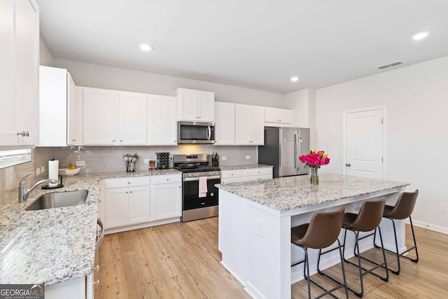 kitchen with backsplash, a kitchen island, light wood-type flooring, stainless steel appliances, and a sink