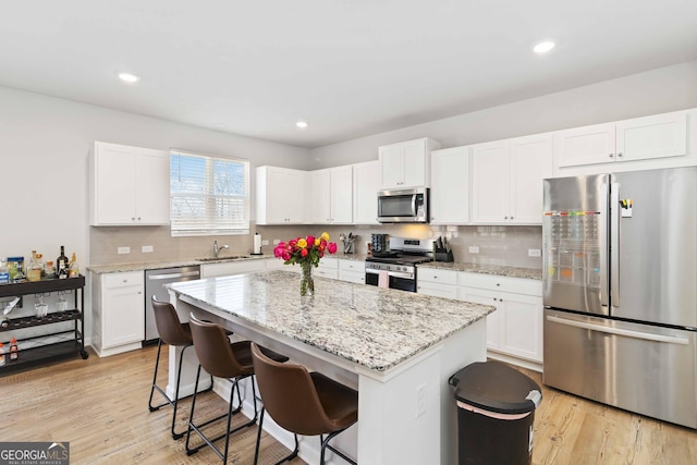 kitchen featuring light wood-style floors, a kitchen island, appliances with stainless steel finishes, and a sink