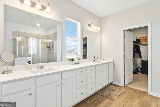 bathroom with double vanity, a shower stall, wood finished floors, and a sink