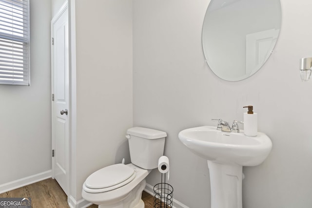 half bathroom with toilet, wood finished floors, baseboards, and a sink