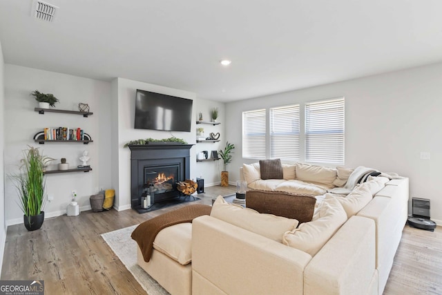 living area featuring visible vents, baseboards, a fireplace with flush hearth, and wood finished floors