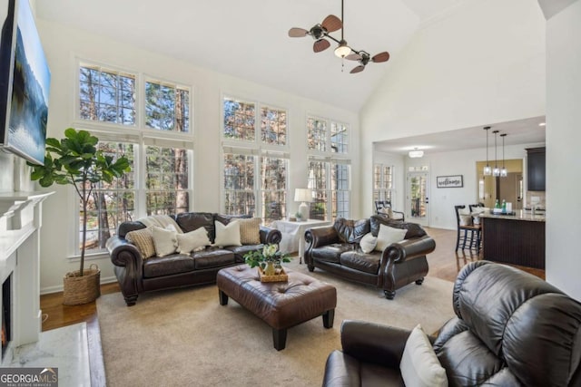 living room with ceiling fan with notable chandelier, a fireplace, high vaulted ceiling, and baseboards