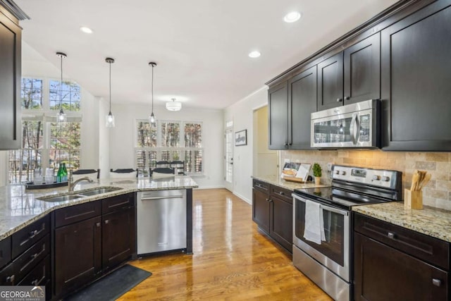 kitchen featuring tasteful backsplash, light wood-type flooring, appliances with stainless steel finishes, hanging light fixtures, and a sink