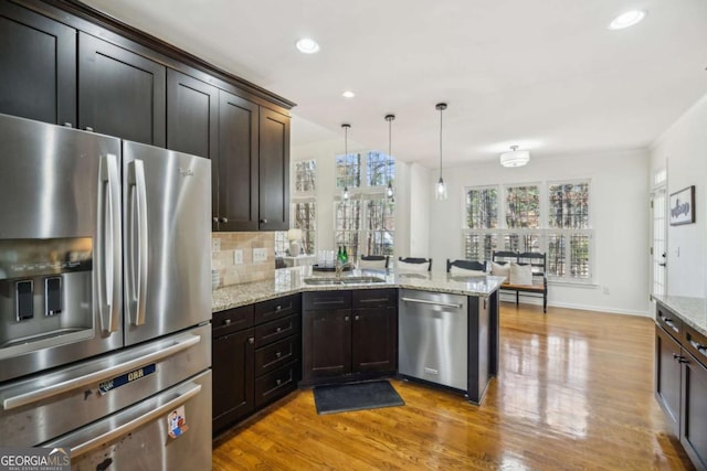 kitchen featuring a peninsula, light wood-style flooring, backsplash, and stainless steel appliances