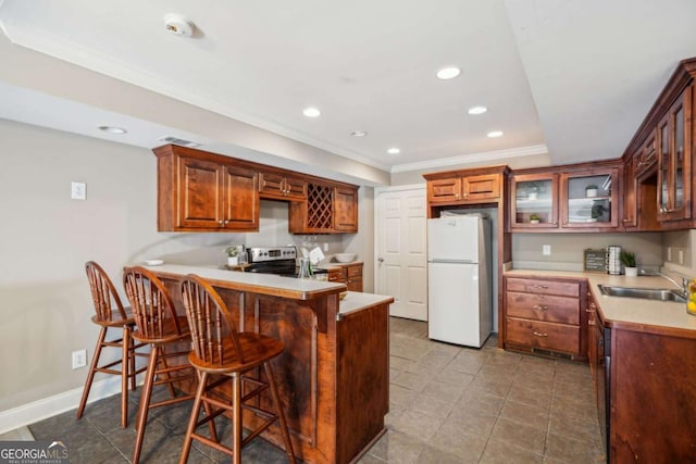 kitchen with glass insert cabinets, stainless steel range with electric cooktop, a peninsula, freestanding refrigerator, and a sink