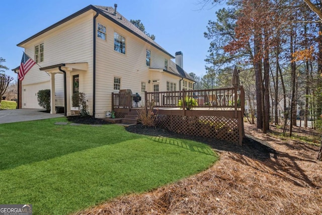 rear view of house featuring an attached garage, a wooden deck, a lawn, a chimney, and driveway