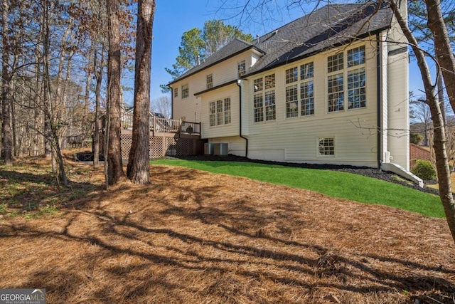 rear view of house featuring a deck, central air condition unit, and a lawn