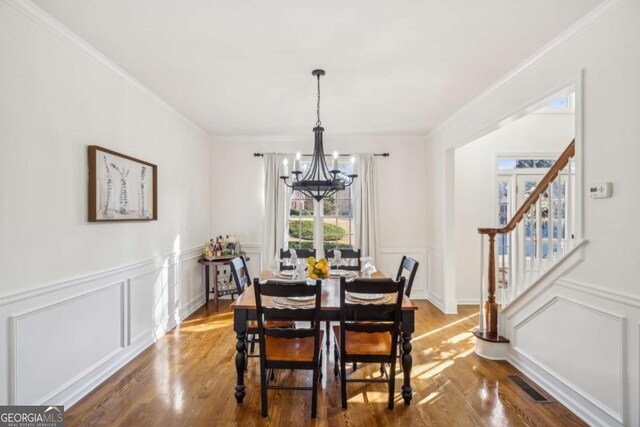 dining space featuring visible vents, crown molding, stairs, an inviting chandelier, and wood finished floors