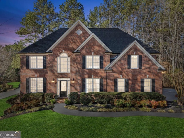 view of front of house with brick siding, a lawn, an attached garage, and a shingled roof