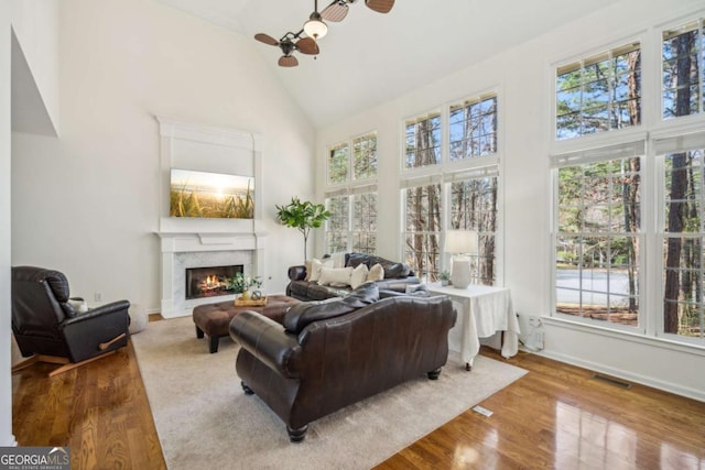 living area featuring visible vents, high vaulted ceiling, a ceiling fan, wood finished floors, and a lit fireplace