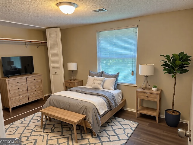 bedroom featuring visible vents, baseboards, wood finished floors, a closet, and a textured ceiling