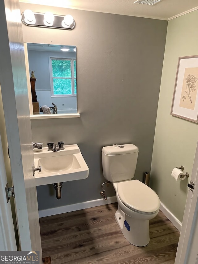 bathroom with toilet, wood finished floors, baseboards, and a sink