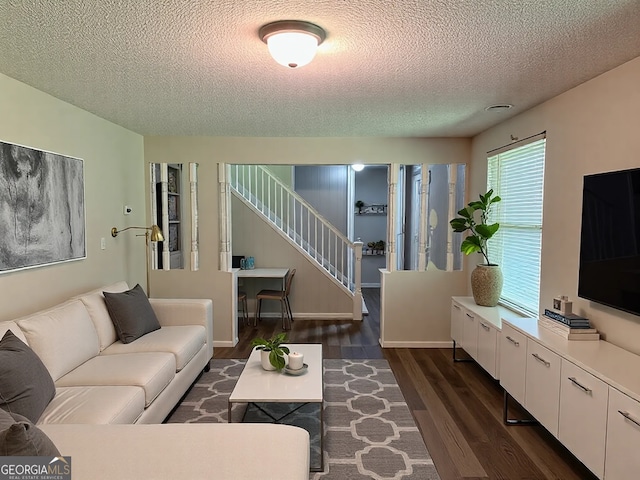 living area with baseboards, a textured ceiling, dark wood-style floors, and stairs