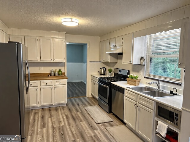 kitchen featuring under cabinet range hood, light wood-type flooring, wainscoting, stainless steel appliances, and a sink