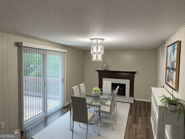 dining area featuring a fireplace with raised hearth, a textured ceiling, dark wood finished floors, an inviting chandelier, and baseboards