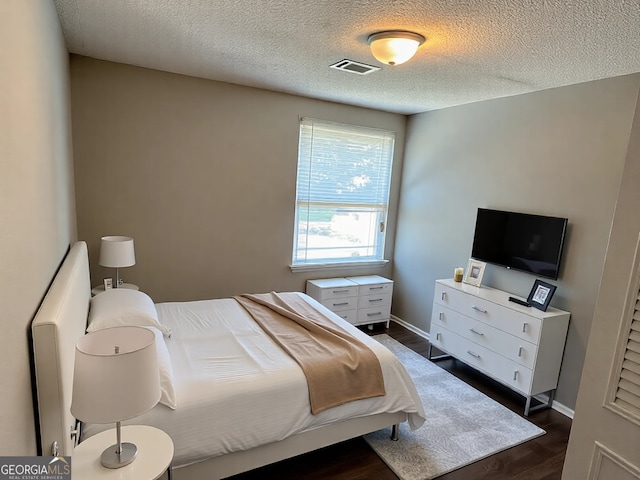 bedroom with visible vents, a textured ceiling, baseboards, and dark wood-style flooring