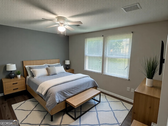 bedroom with visible vents, baseboards, wood finished floors, a textured ceiling, and a ceiling fan