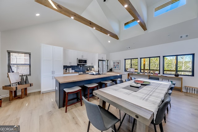 dining space featuring beamed ceiling, plenty of natural light, visible vents, and light wood-type flooring