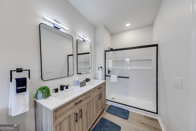 bathroom with a stall shower, a sink, wood finished floors, recessed lighting, and double vanity