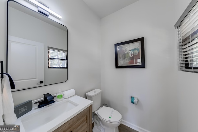 half bath featuring baseboards, toilet, and vanity