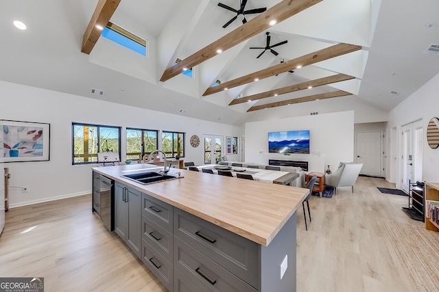 kitchen featuring beamed ceiling, a kitchen island with sink, gray cabinets, a sink, and open floor plan