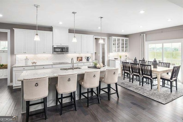 kitchen featuring stainless steel microwave, an island with sink, dark wood-style floors, white cabinets, and a sink