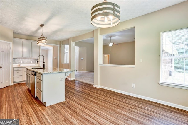 kitchen with a sink, backsplash, baseboards, wood finished floors, and stainless steel dishwasher