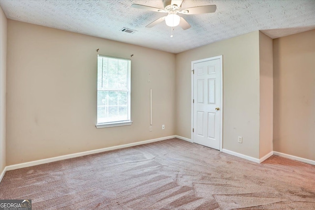 empty room featuring visible vents, a textured ceiling, carpet floors, baseboards, and ceiling fan